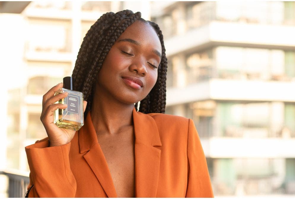 Jovem negra segurando o perfume Fava Tonka com olhos fechados e semblante tranquilo e delicadamente feliz